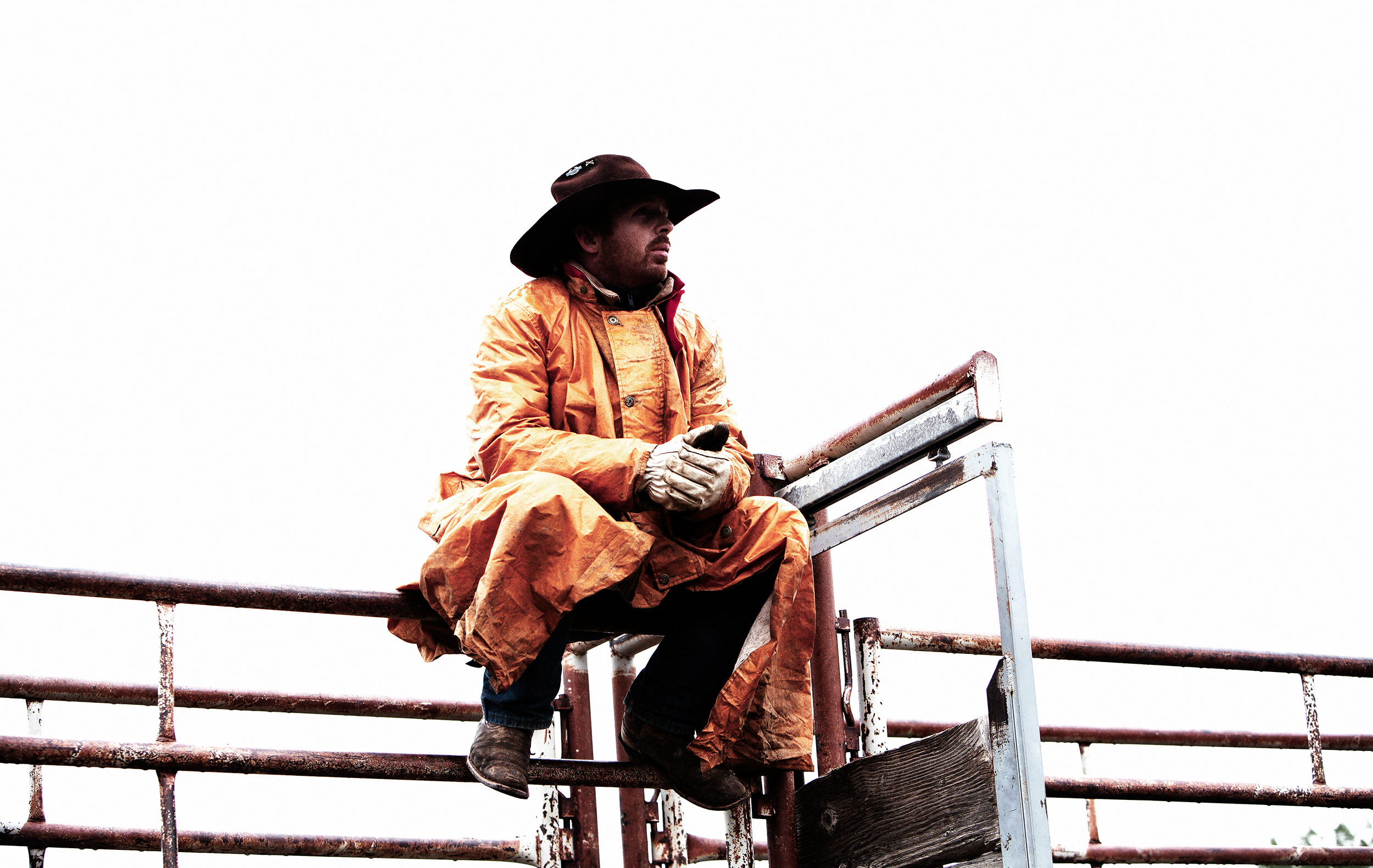 Cowboy wearing a yellow rain slicker while sitting on a metal corral at a rodeo