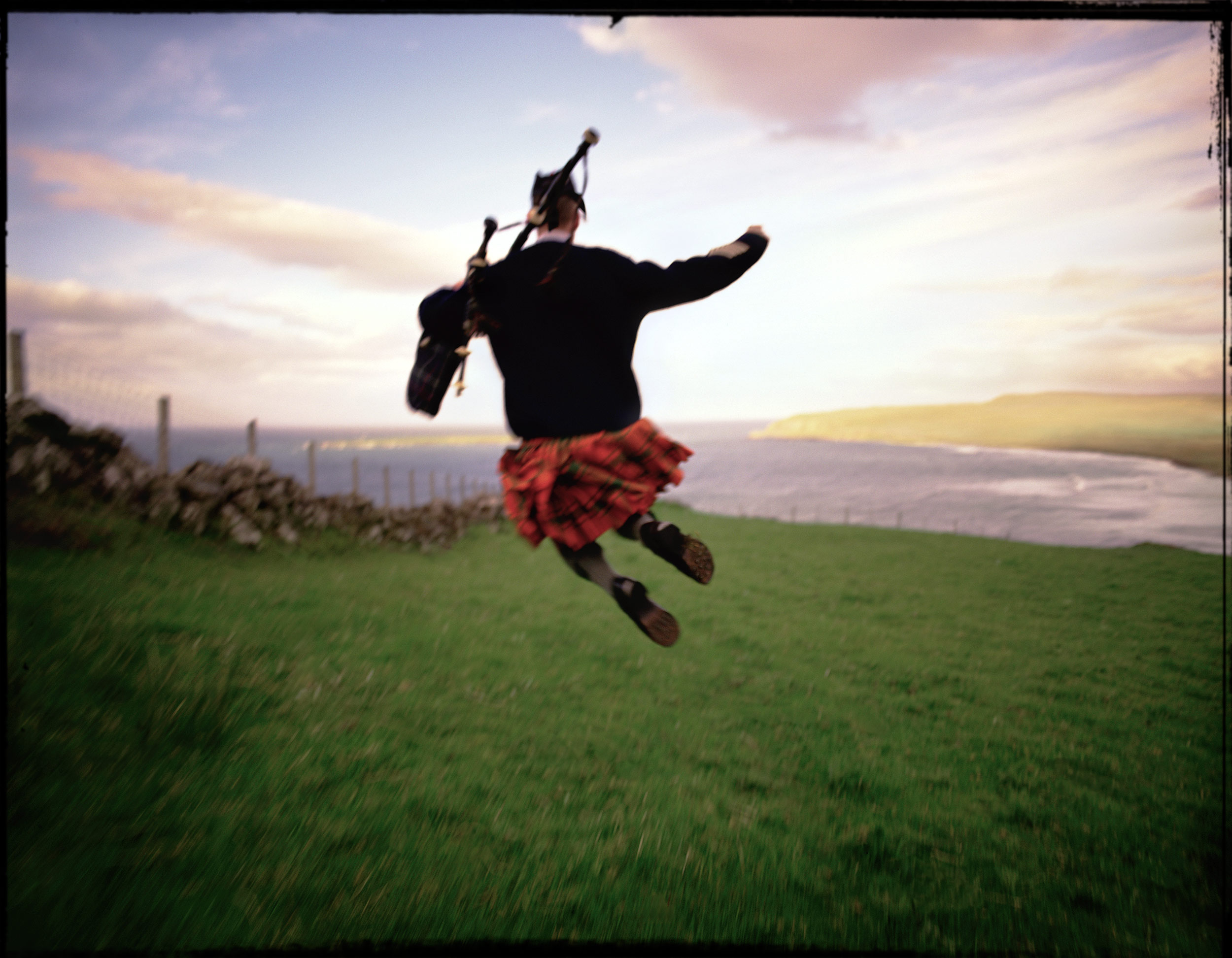 Bagpiper jumping in the air in a green pasture on the Isle of Skye, Scotland